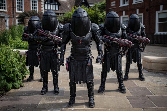 This image shows five Judoon soldiers standing in a diamond-head formation on the grounds of Gloucester, England's village cathedral. Four Judoon brandish large laser guns while their commander holds a genetic scanning device.