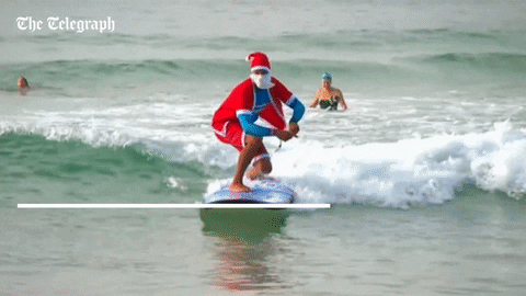 A man in a Santa suit and a large beard surfs a large wave.