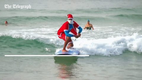 A man in a Santa suit and a large beard surfs a large wave. A man in a Santa suit and a large beard surfs a large wave.