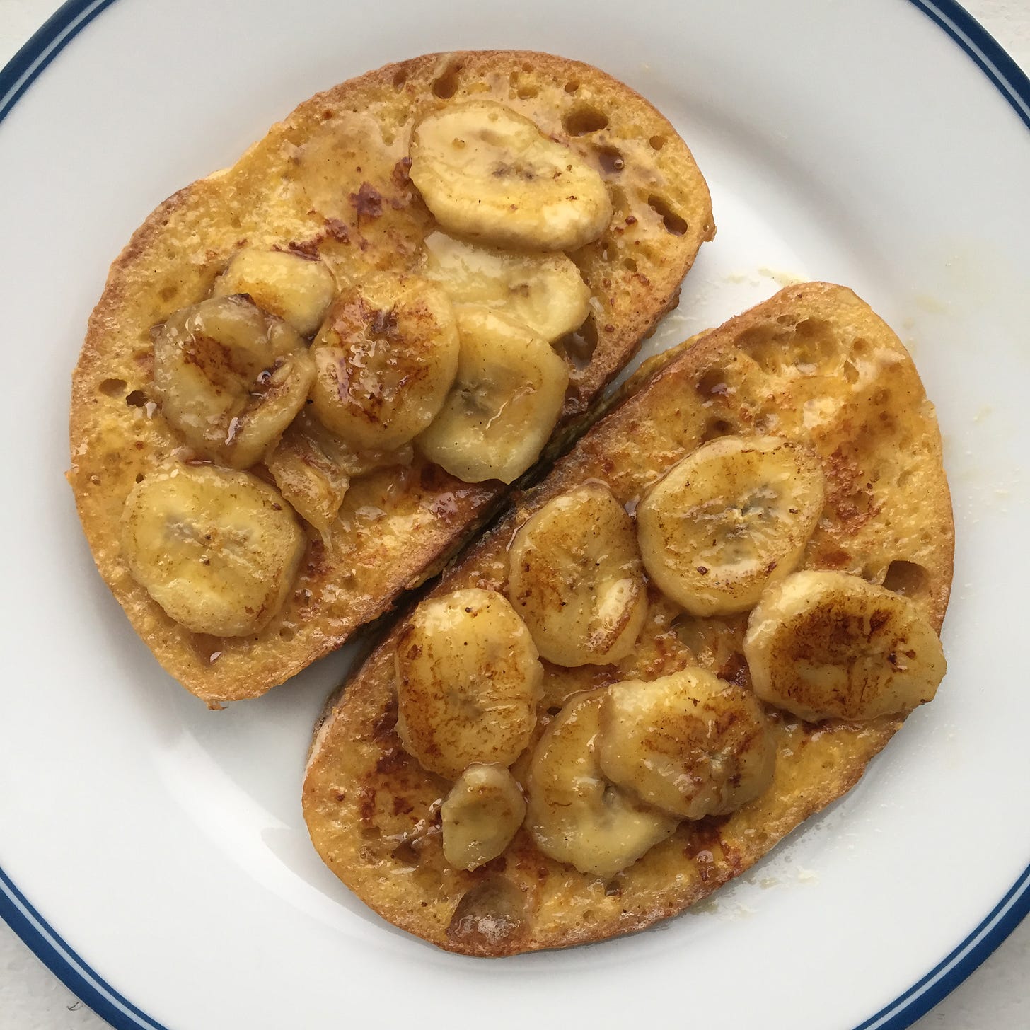 Two slices of French toast covered in syrup and bananas, on a white plate.