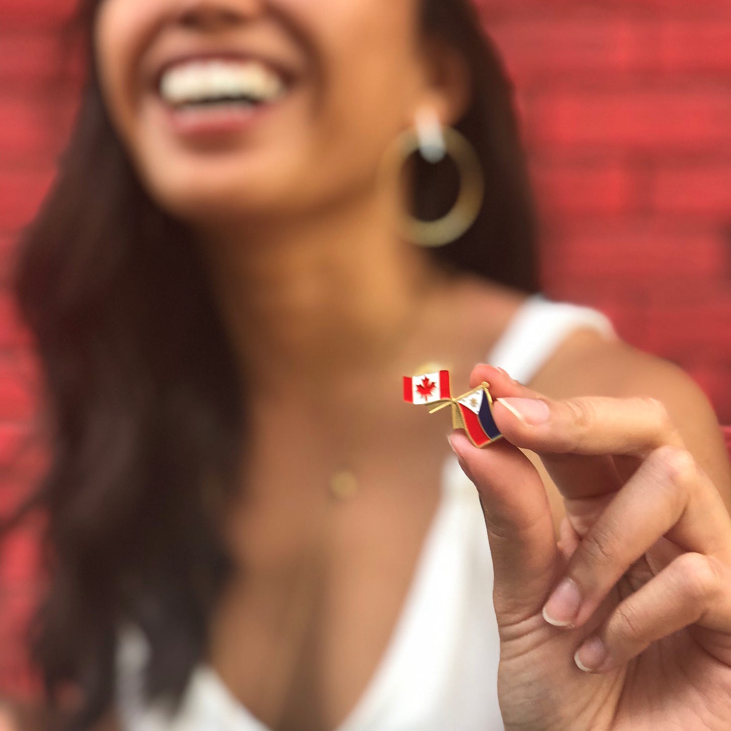 Justine's face blurred while she holds up a small pin with the Philippines and Canadian flag.