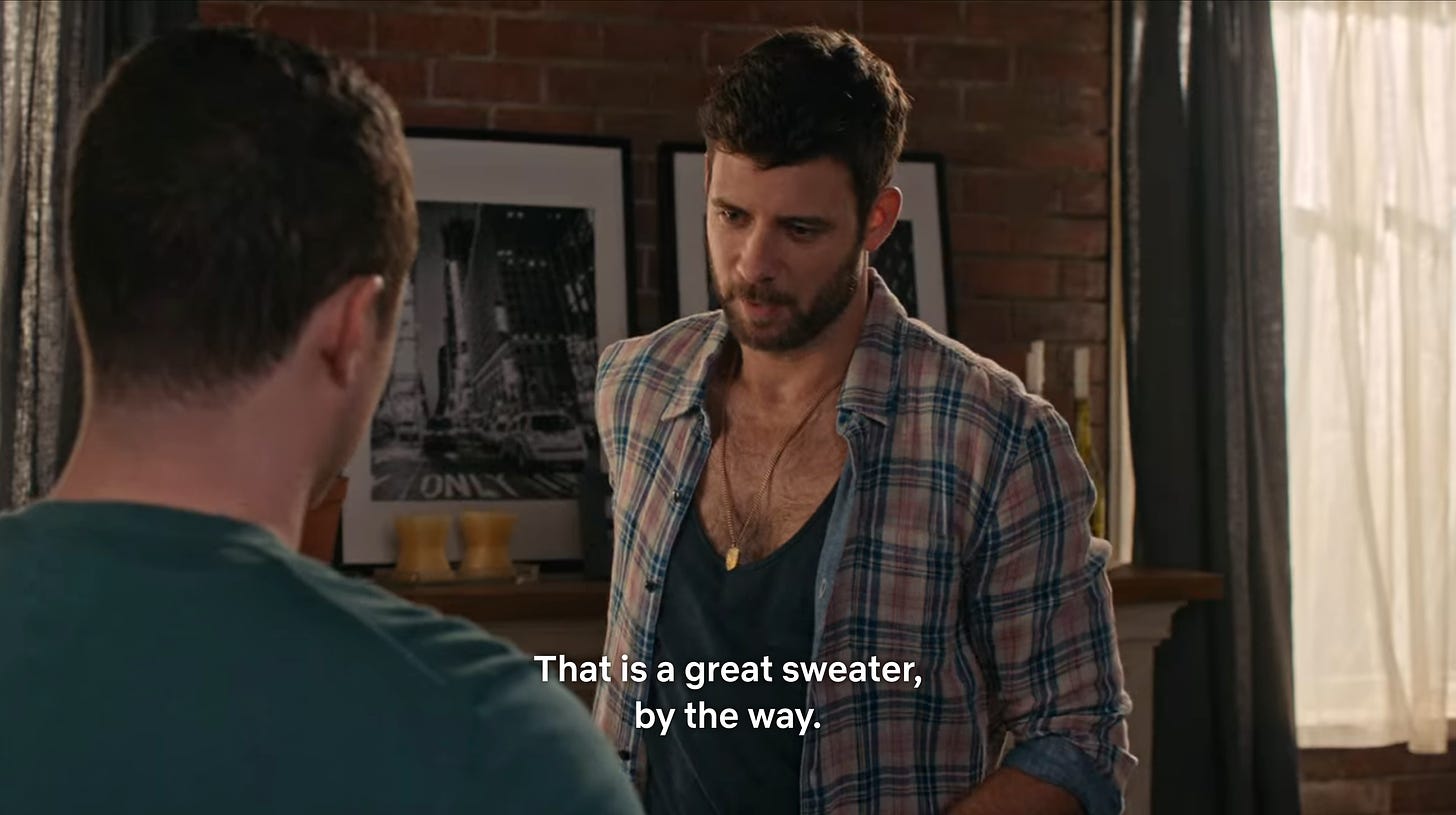 Patrick (left) and Jake (right) in SCHITT'S CREEK. Jake, looking down at Patrick's sweater, tells him, "That is a great sweater, by the way."