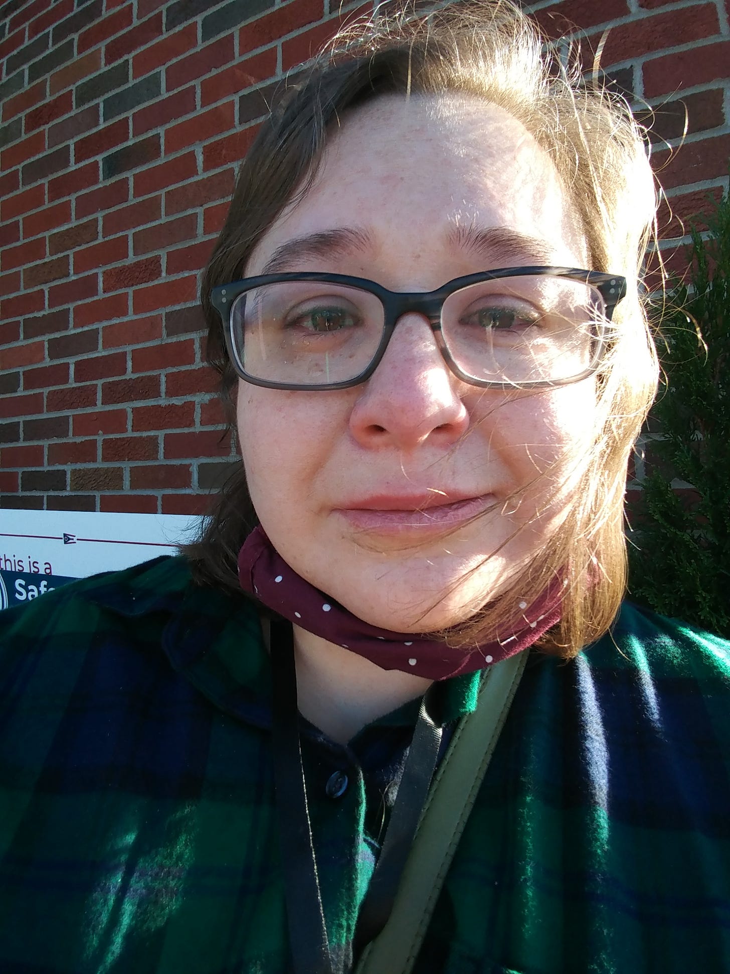 A teary-eyed Lyndsey wearing glasses and a flannel shirt, with her mask pulled under her chin.
