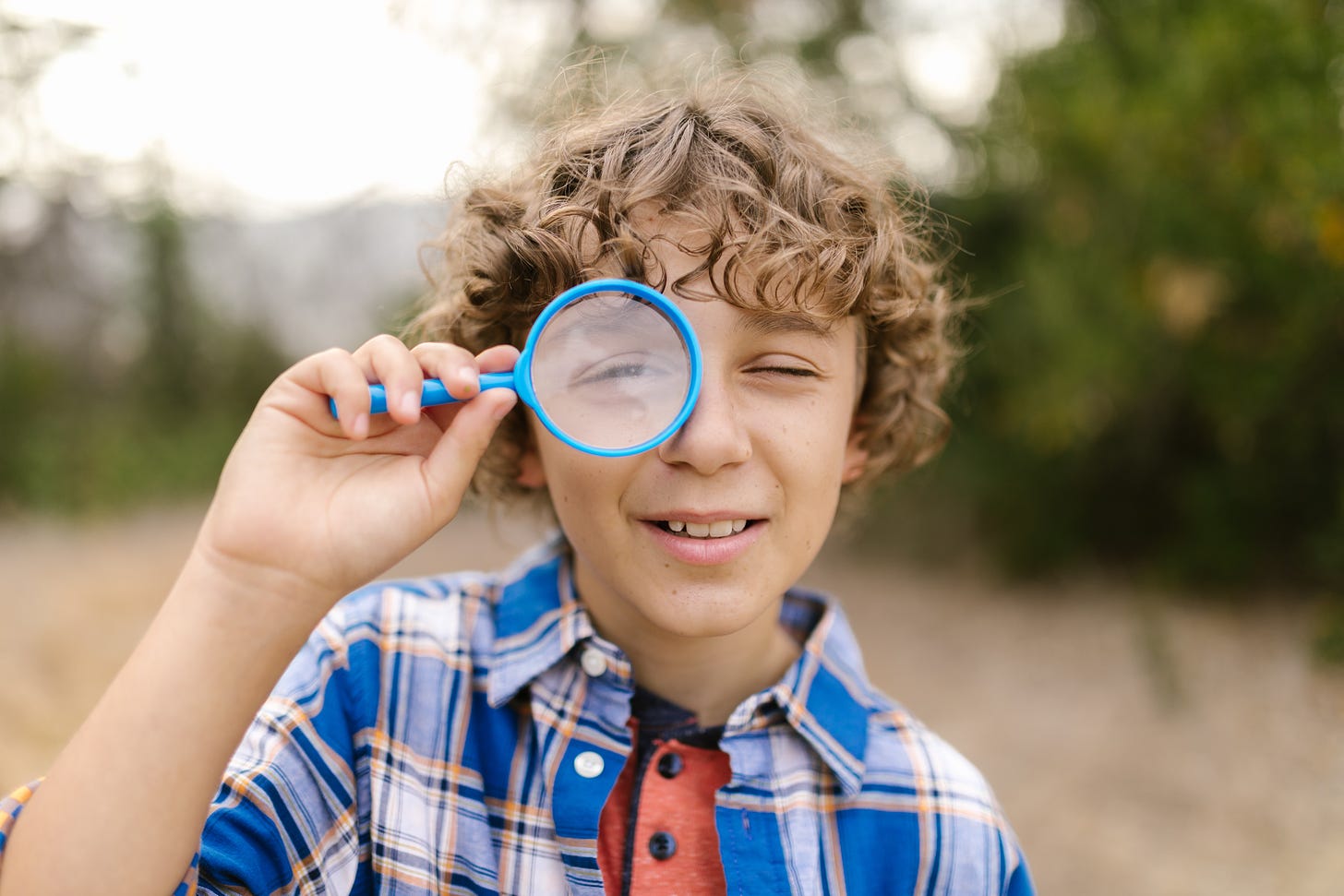 Boy with brown curly hair looking through a blue magnifying glass.