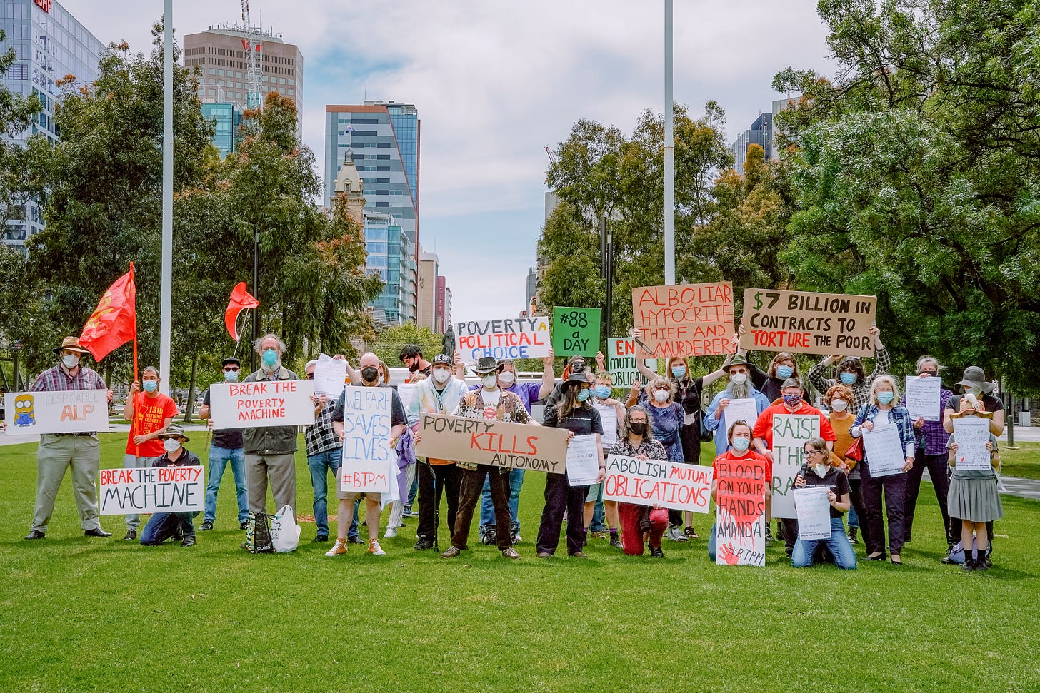 A crowd in a park holding protest signs. 