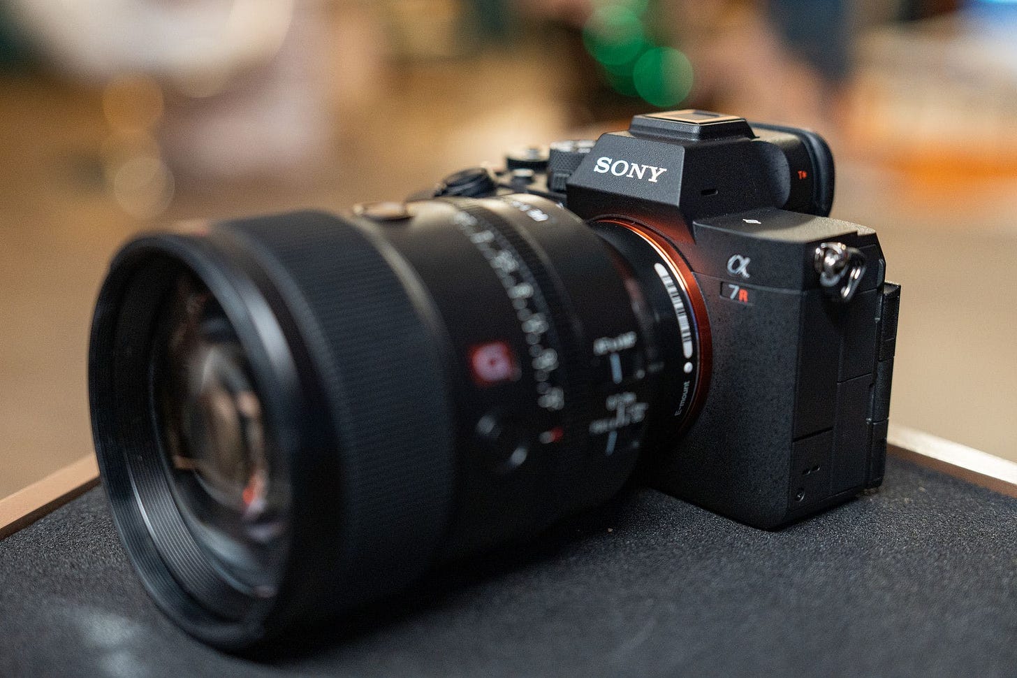 The Sony A7R V camera sitting on a counter with a lens attached to it, in front of a blurred-out background.