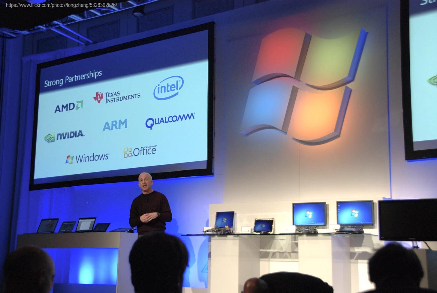 Event photo with author on stage showing a slide "Strong Partners" with logos from AMD, Texas Instruments, Intel, NVIDIA, ARM, Qualcomm, Windows, and Office.