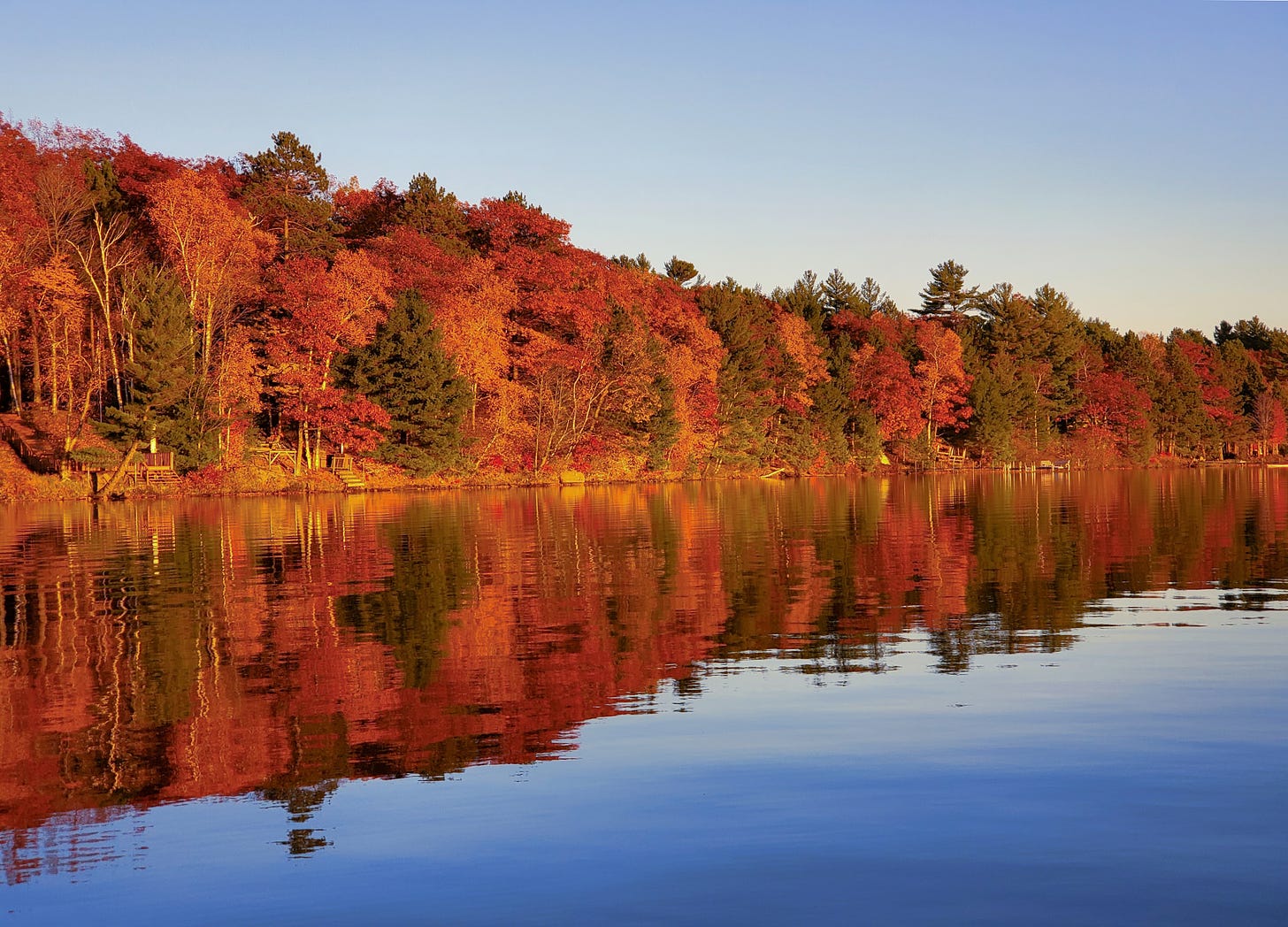 Brightly colored autumn leaves on trees line a placid lake, where the reflected reds, yellows, and greens can be seen clearly in the water, too.