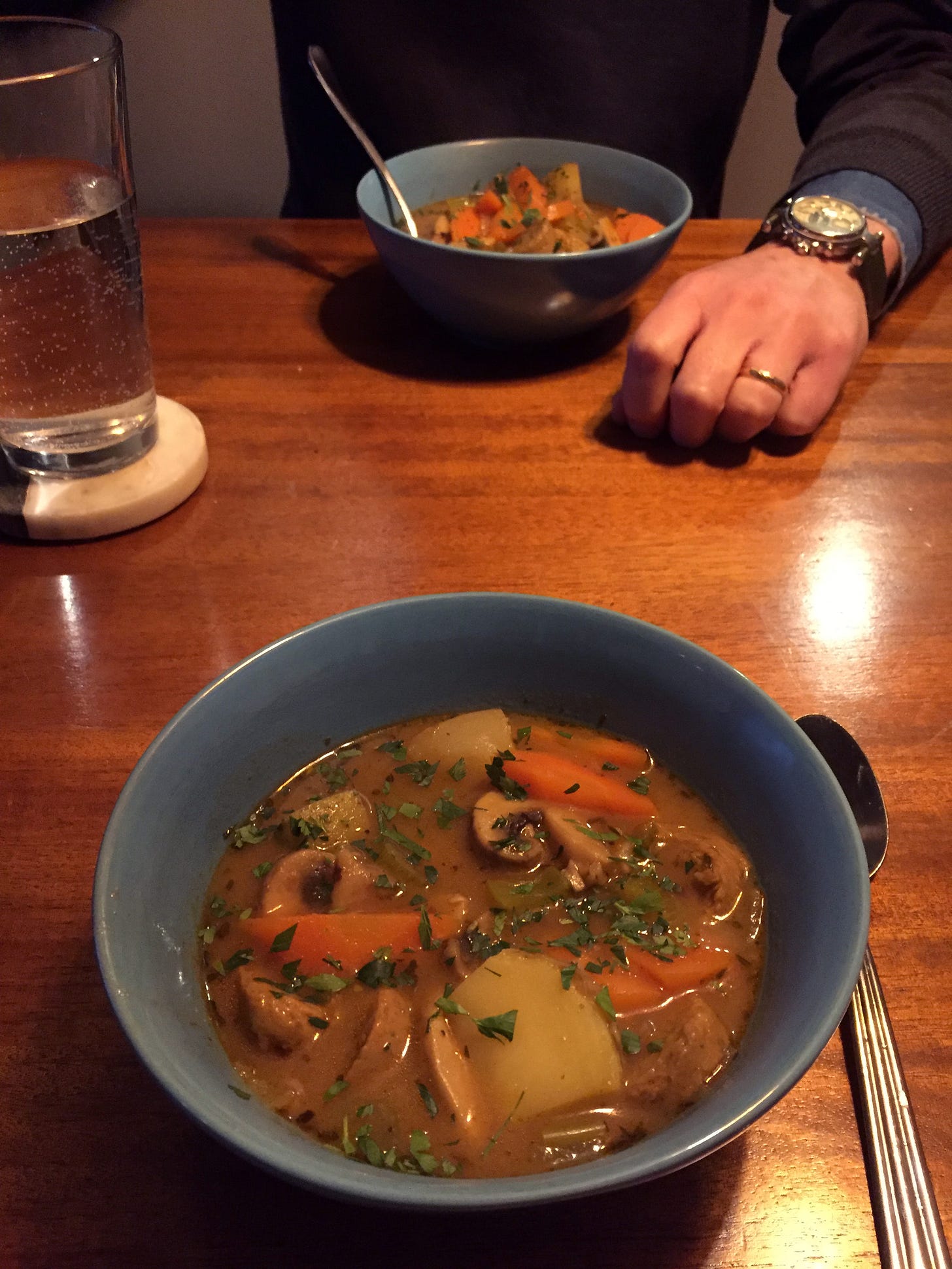 In two blue bowls across from each other, a bowl of stew made with potatoes, carrots, sausage, and mushrooms sprinkled with parsley