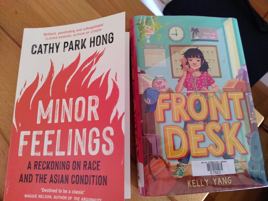 Two book covers, side by side:  1) Minor Feelings by Cathy Park Hong which shows a red set of flames on bottom 2/3rd of book agains white background in top 1/3rd and 2) Front Desk by Kelly Yang shows illustration of girl on the phone standing behind an improvised reception desk. hotel 