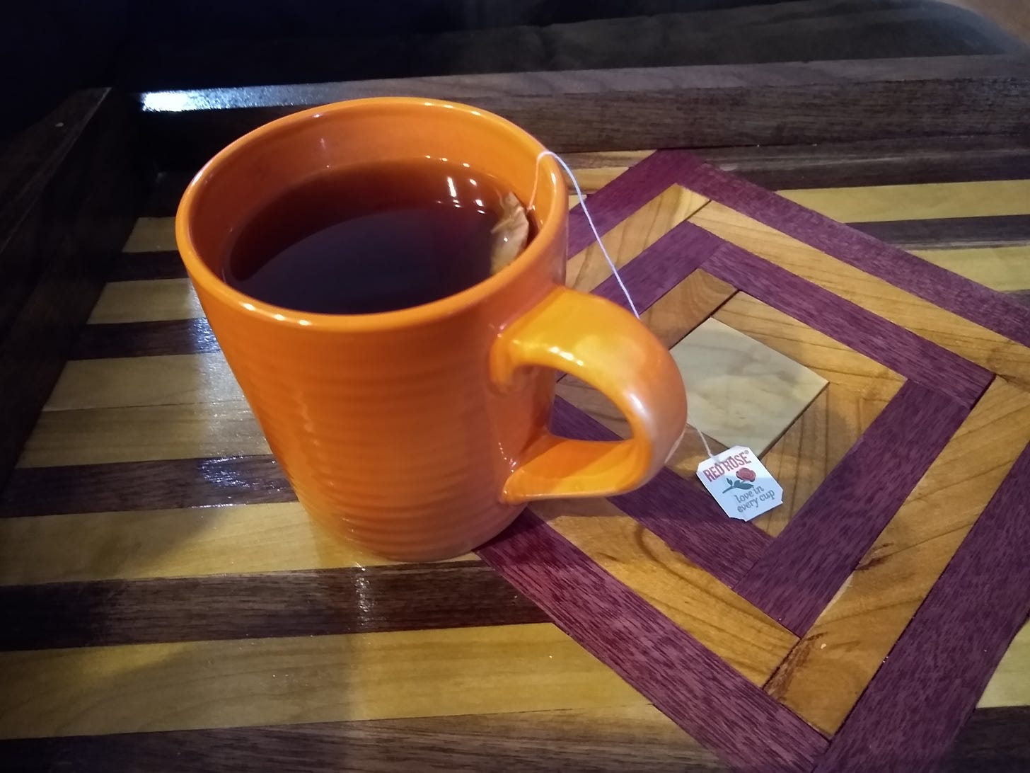 Red Rose black tea in an orange mug on a wooden tray