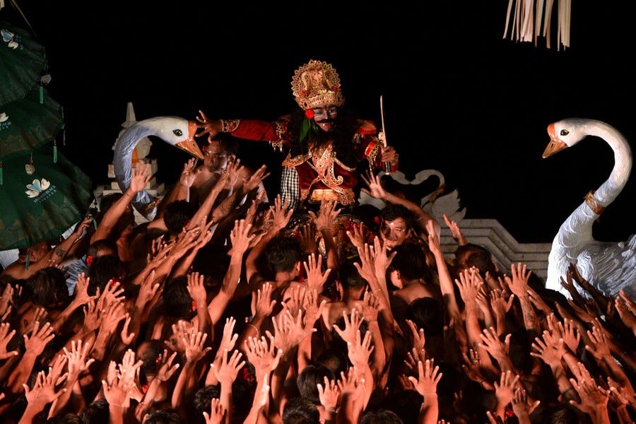 Dozens of outstretched hands reach up toward a performer in costume during a dance performance.