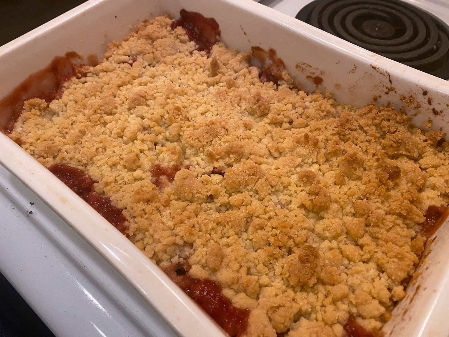 a rectangular white baking dish with a golden-brown crumble in it. Pinkish juices have bubbled up at the edges.