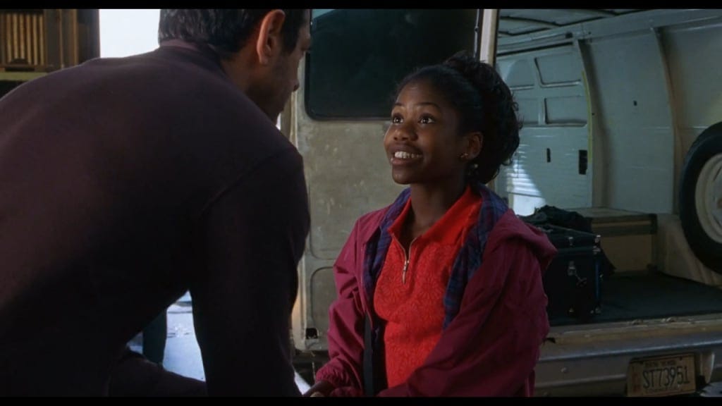 an eleven year old Black girl smiles gorgeously, wearing a red shirt and burgundy zip-up. She looks into her father's face, who has his back to the camera and is wearing a black long-sleeved knit.