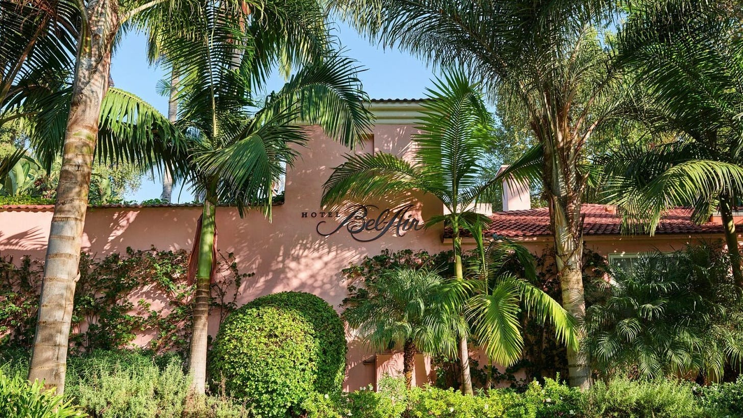 Hotel exterior with logo sign, pink building and trees