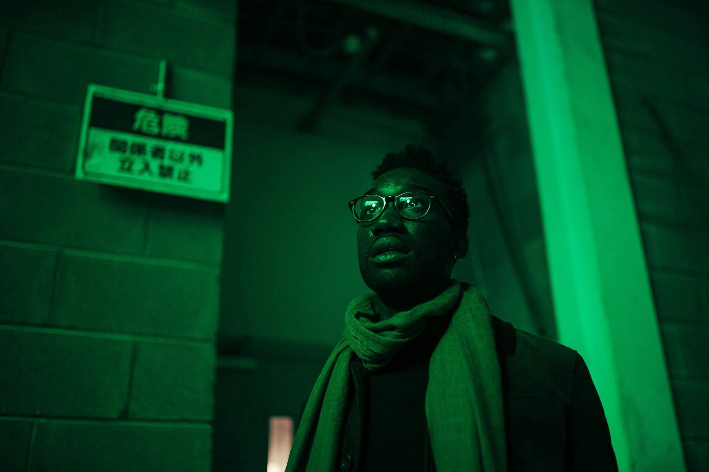 This image shows Leo Rugazzi (played by Nathan Stewart-Jarratt) staring up and off-camera at the unseen Dalek clone farm he's inadvertently built in Osaka, Japan. The image is suffused in green light, while Leo stands near a sign written in Japanese. This image shows Leo Rugazzi (played by Nathan Stewart-Jarratt) staring up and off-camera at the unseen Dalek clone farm he's inadvertently built in Osaka, Japan. The image is suffused in green light, while Leo stands near a sign written in Japanese.