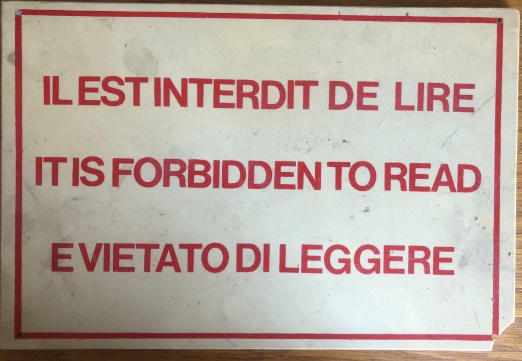 A white plastic sign with red writing in block capitals: "IL EST INTERDIT DE LIRE. IT IS FORBIDDEN TO READ. E VIETATO DI LEGGERE."