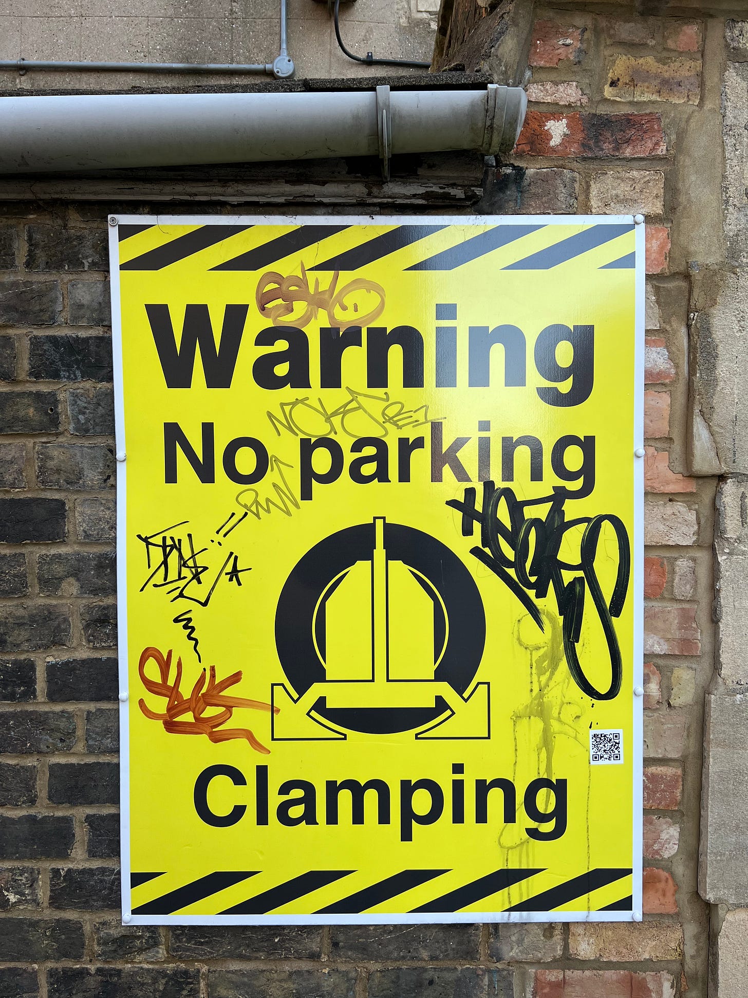 A no parking wheel clamping sign with some graffiti on it.