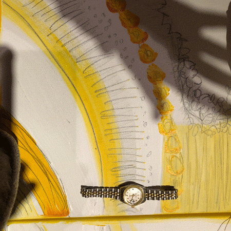 A photo animation of a shadow of hand continually grasping at a silver wrist-watch on a painted white background with pencil sketches and yellow paint lines on top of it. 