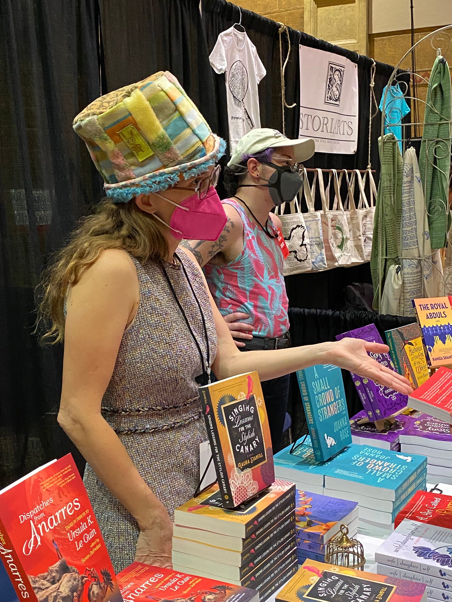 People wearing hats stand behind a table of books. 