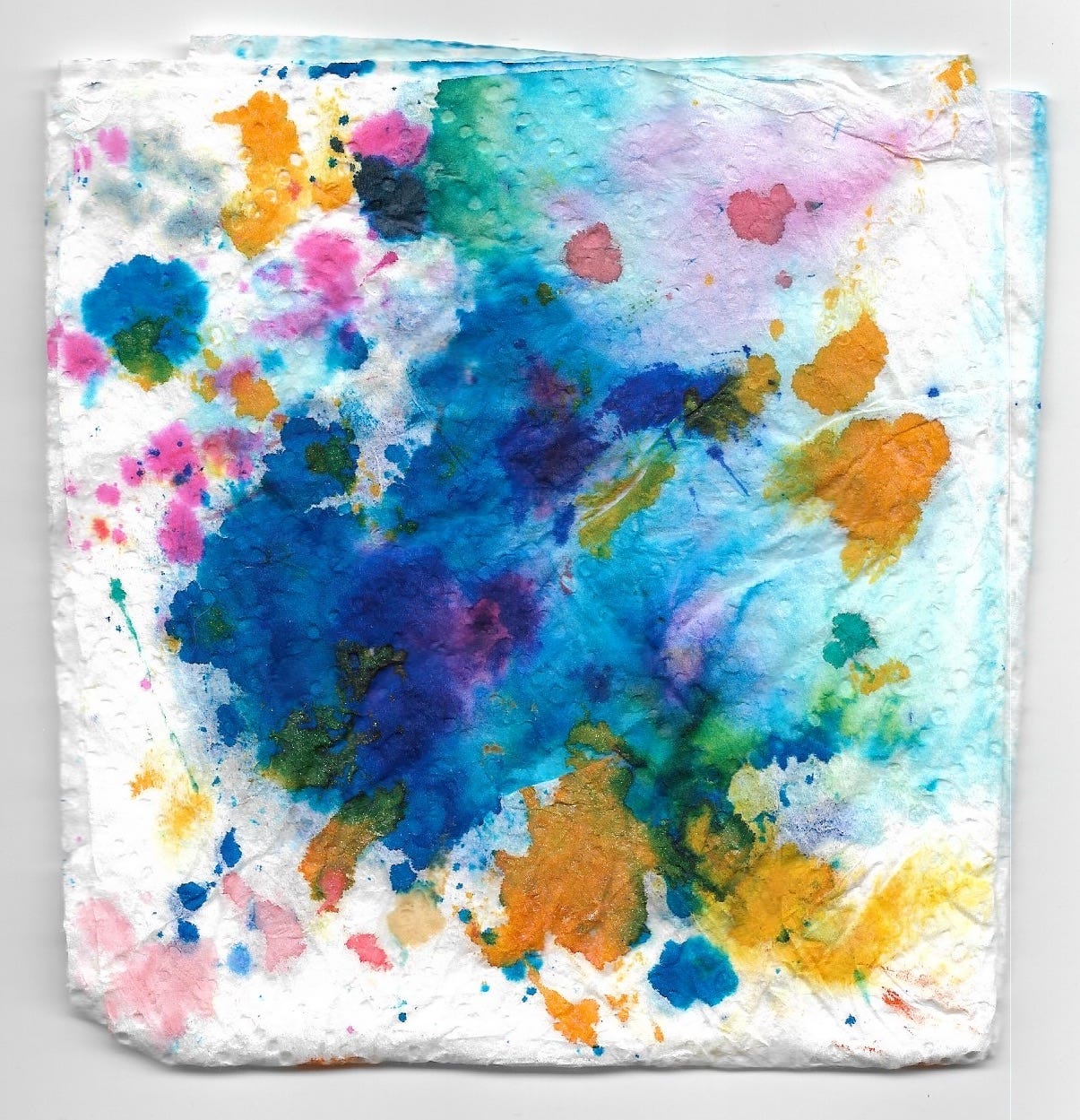 a messily folded piece of paper towel with a bleeding splotch of blue and purple, splattered with gold and pink at the edges