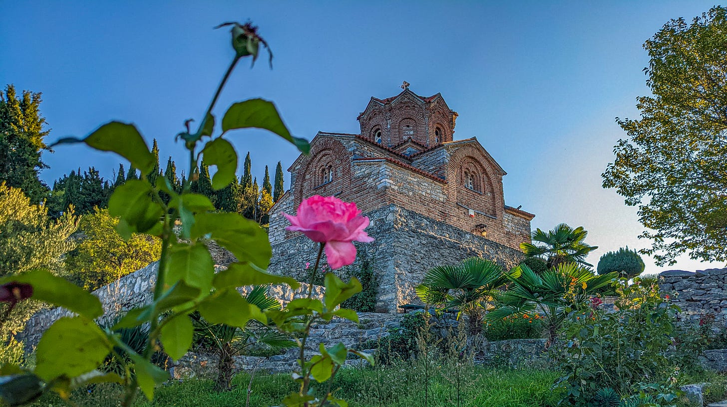 The Church of Saint John the Theologian shot from below, a single pink rose in the foreground.