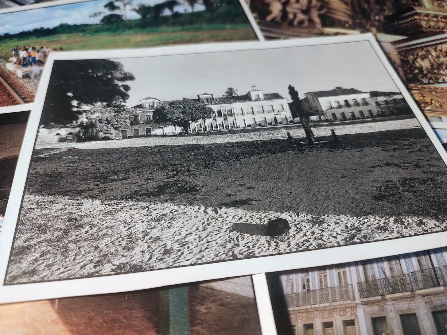 cartão postal com foto em preto e branco da praça Matriz em Alcântara, um descampado com um pelourinho no canto direito. ao fundo, casarões coloniais