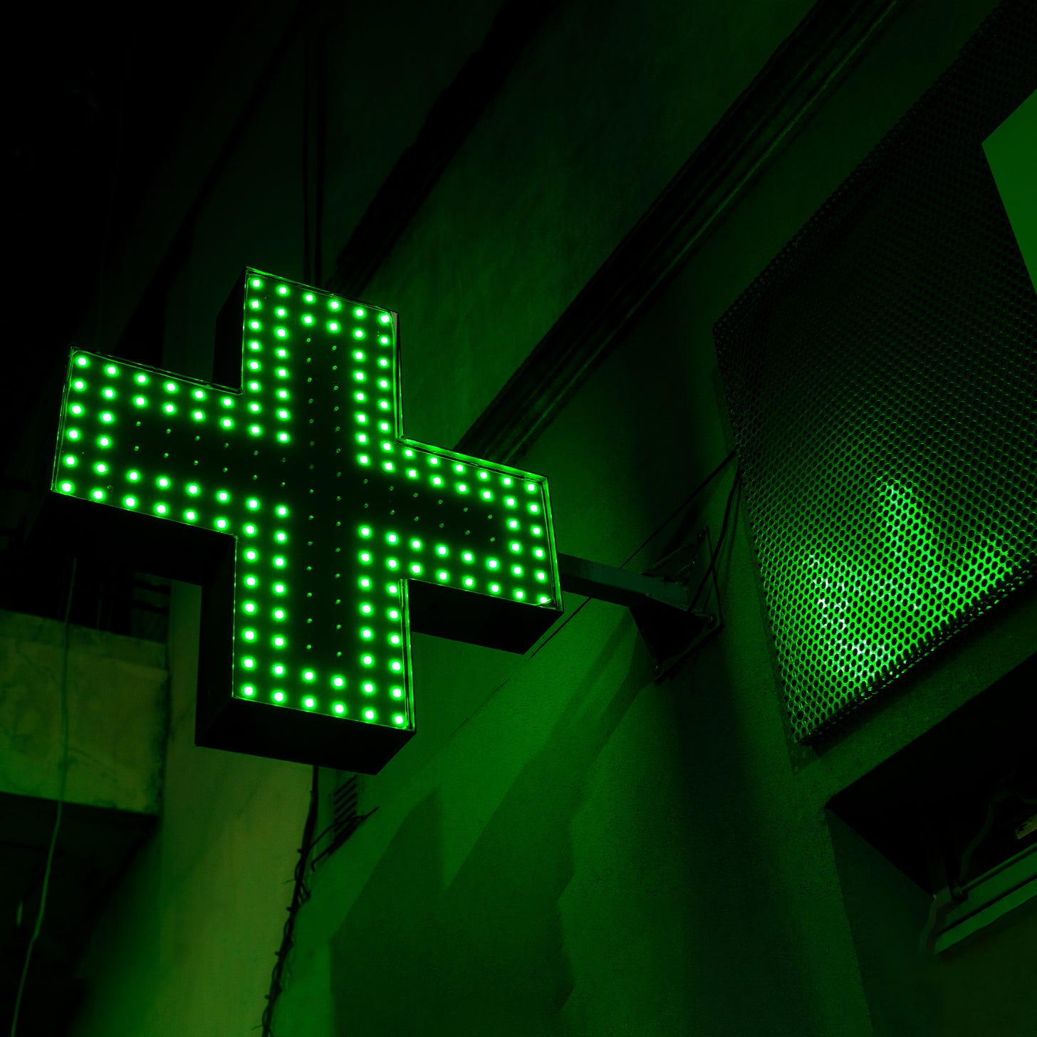 An illuminated green cross pharmacy sign.
