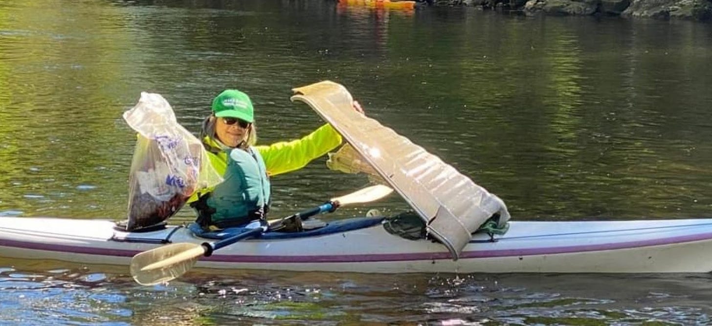 Amy Hall in a kayak, on a river, holding up bags of trash