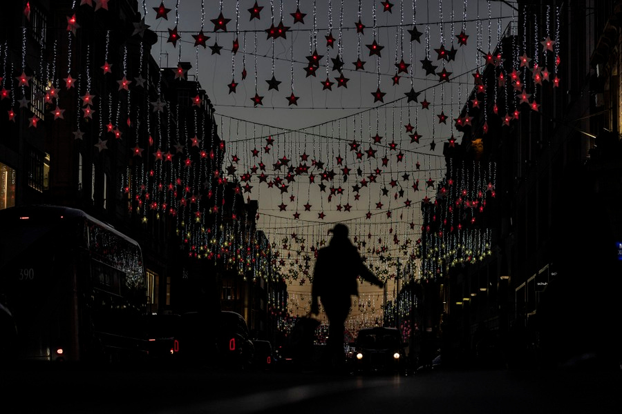 People walk and drive ina street decorated with hundreds of red lit stars hanging from lines across the road.
