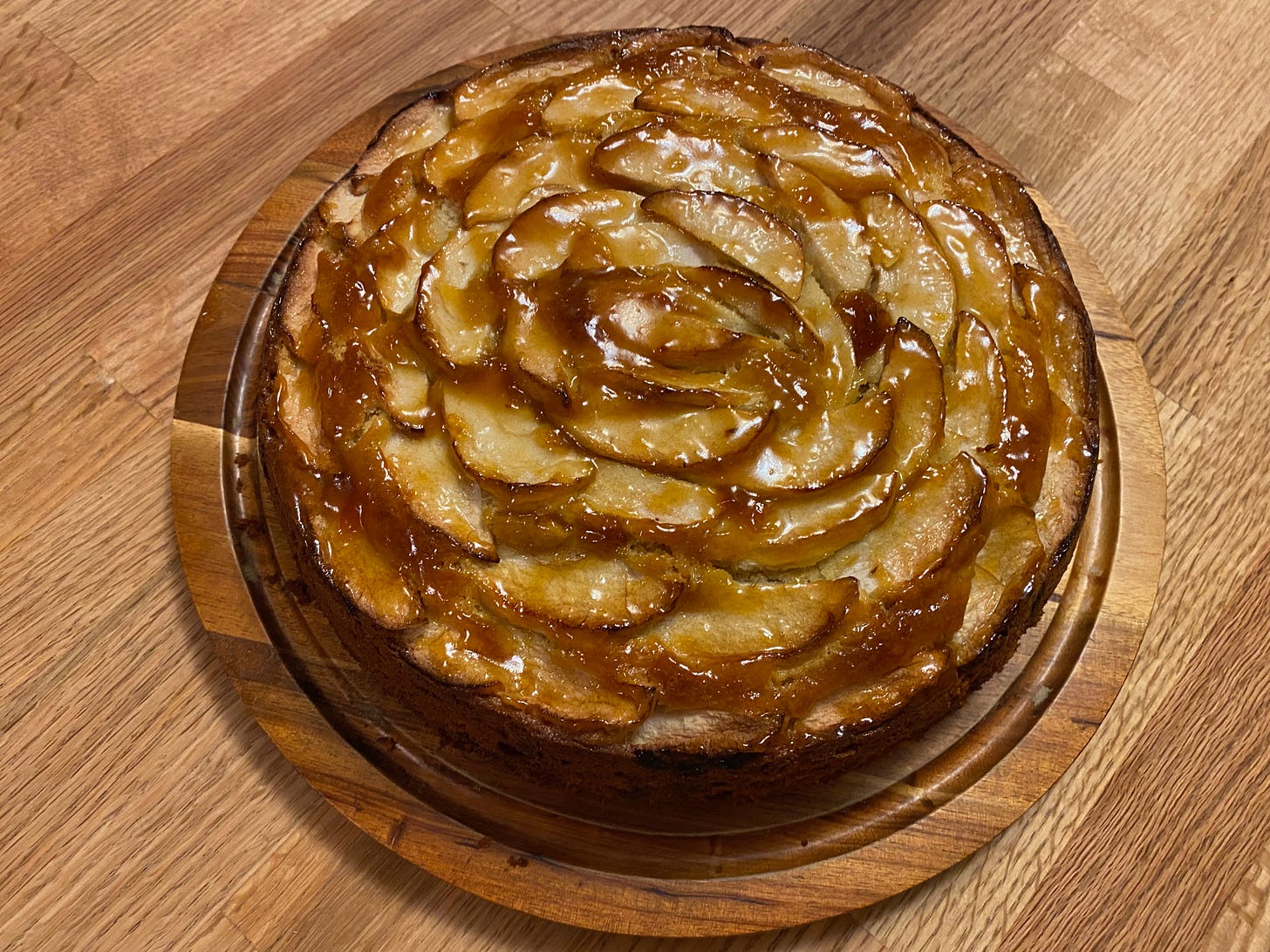 A round cake topped with apple slices arranged in concentric overlapping circles, shiny with apricot glaze.