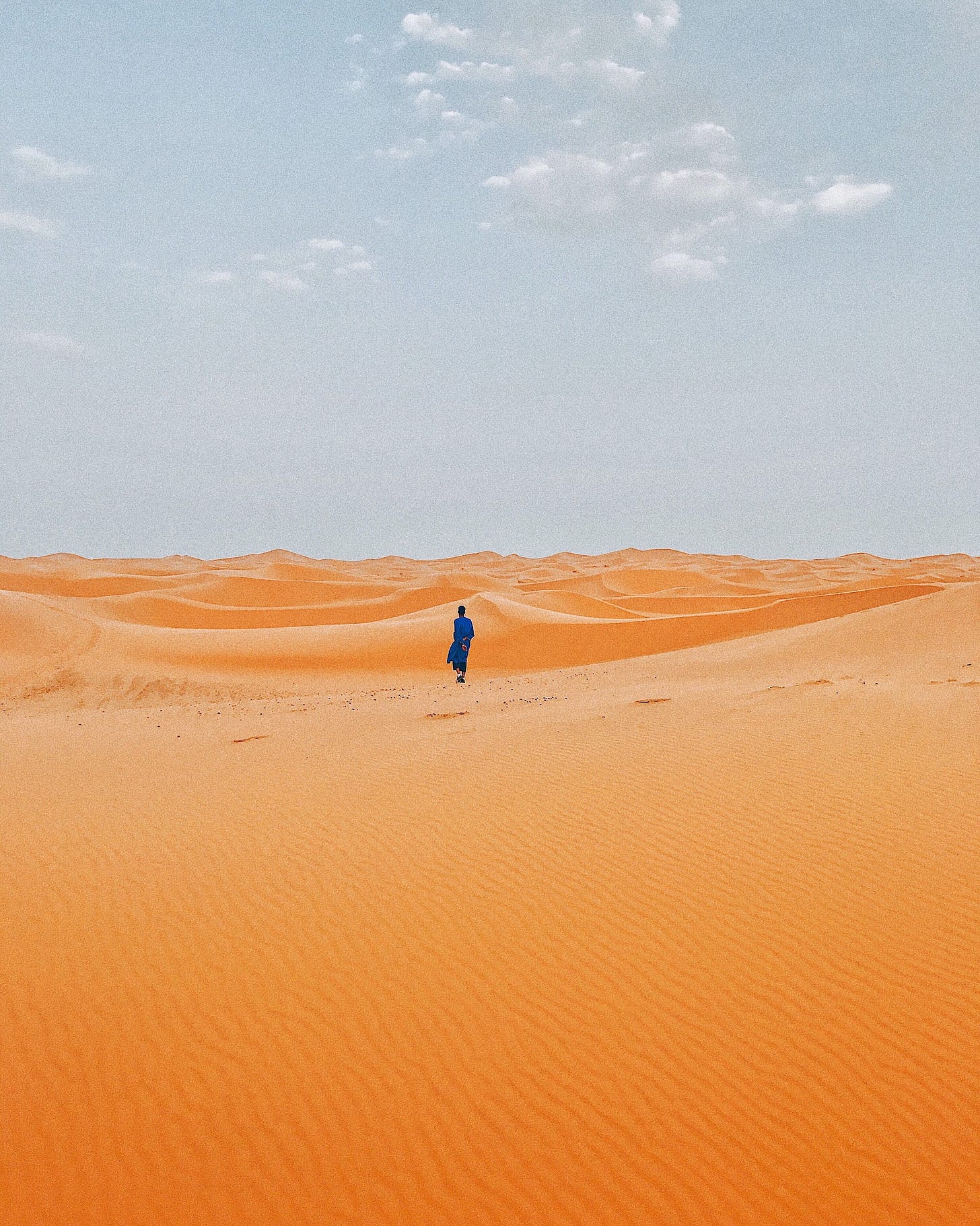 Male human figure striding across wide sand dunes under a clear blue sky