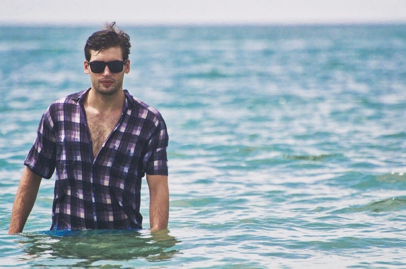 A man wearing a shirt and sunglasses standing in water. 