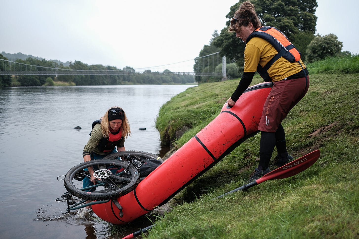 Two people loading a partially disassembled dirt bike onto a packraft.