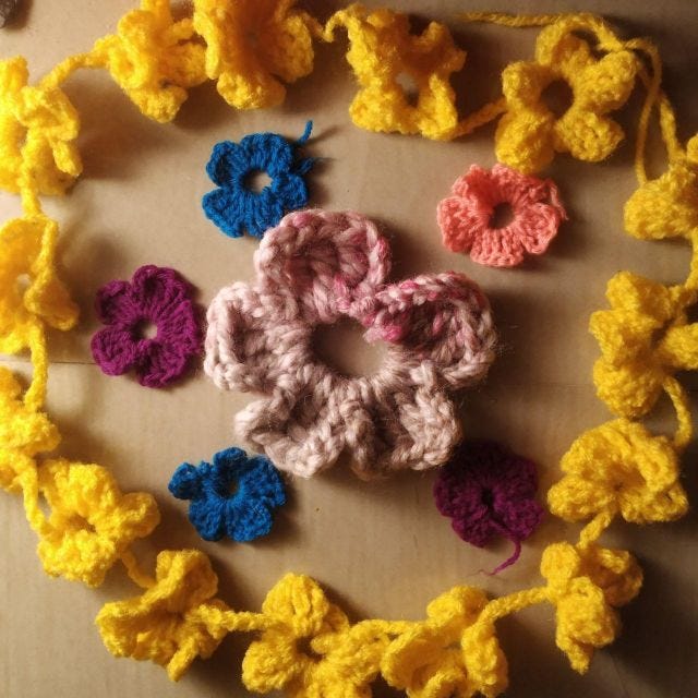 A string of yellow crocheted flowers with other flowers in the middle. all crocheted and in different colours from yellow, to pink to purple to blue.