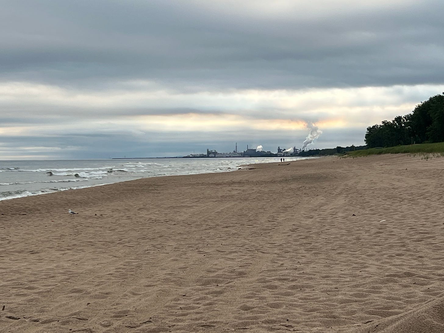 A beach on a cloudy morning with factories and smokestacks in the distance
