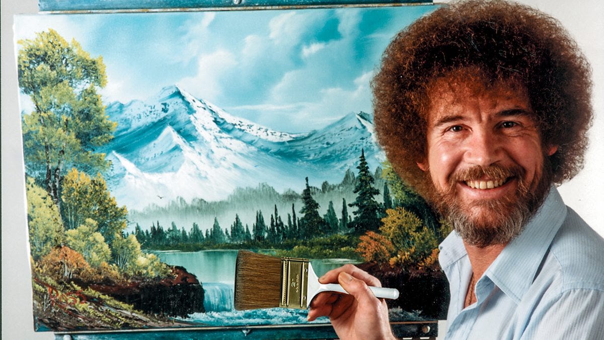 Bob Ross is smiling at the camera, standing in front of a painting of mountains and trees and a lake, holding a paintbrush