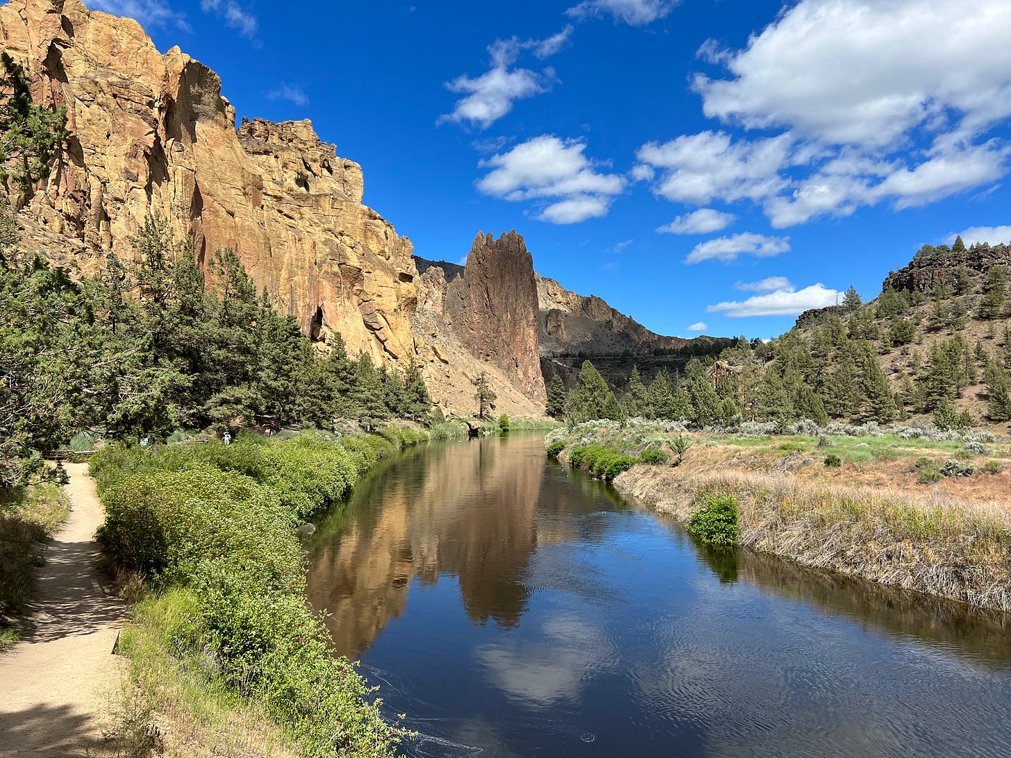 Smith Rock State Park river with a hiking trail next to it and a blue sky with clouds.