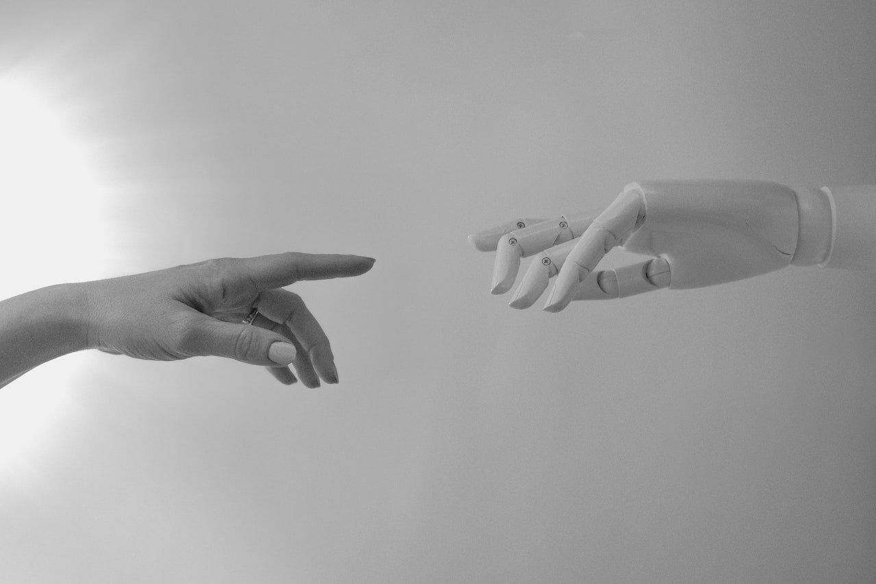 Black and white photo of a human hand touching a robot hand in the style of "The Creation of Adam" painting