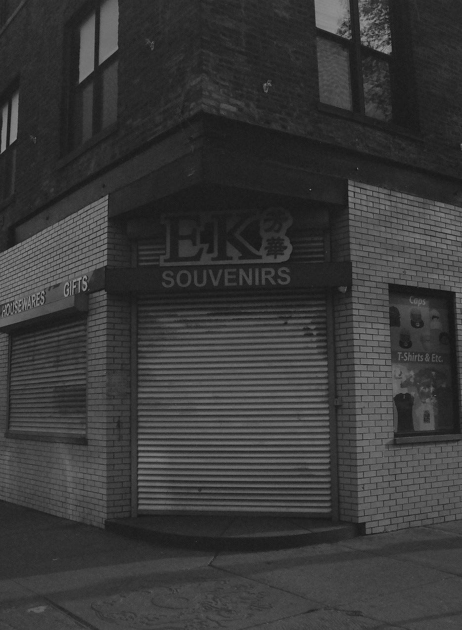 Black and white photograph of store called "EK Souvenirs" with its door closed and an empty sidewalk.