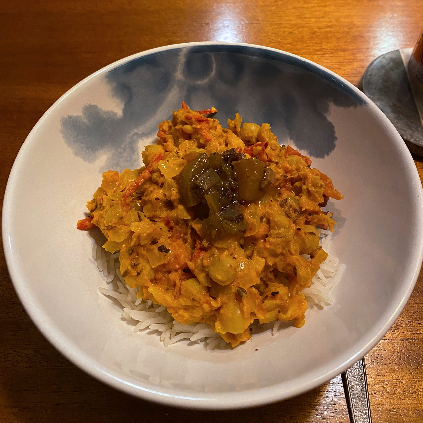 A white and blue bowl with chana masala on top of white basmati rice. A little scoop of chutney sits on top.