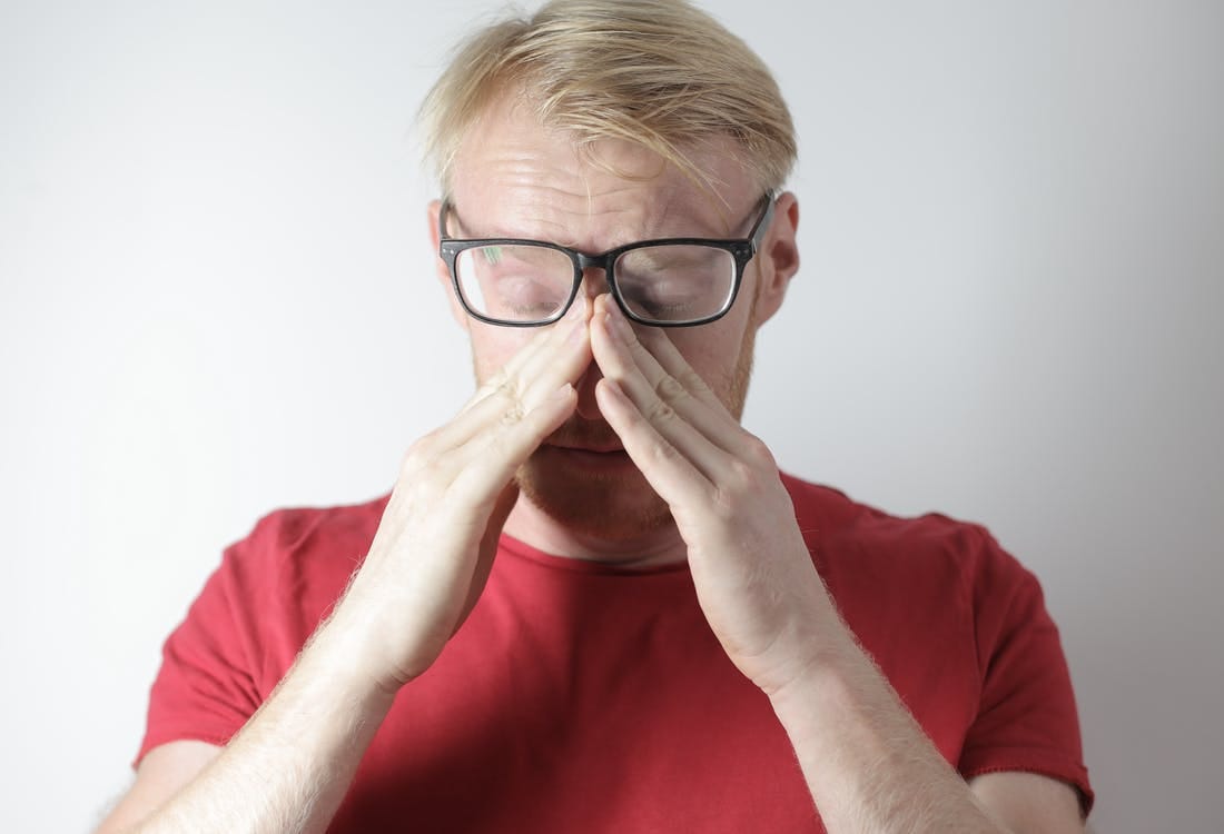 Exhausted mature man rubbing nose bridge after wearing glasses near gray wall