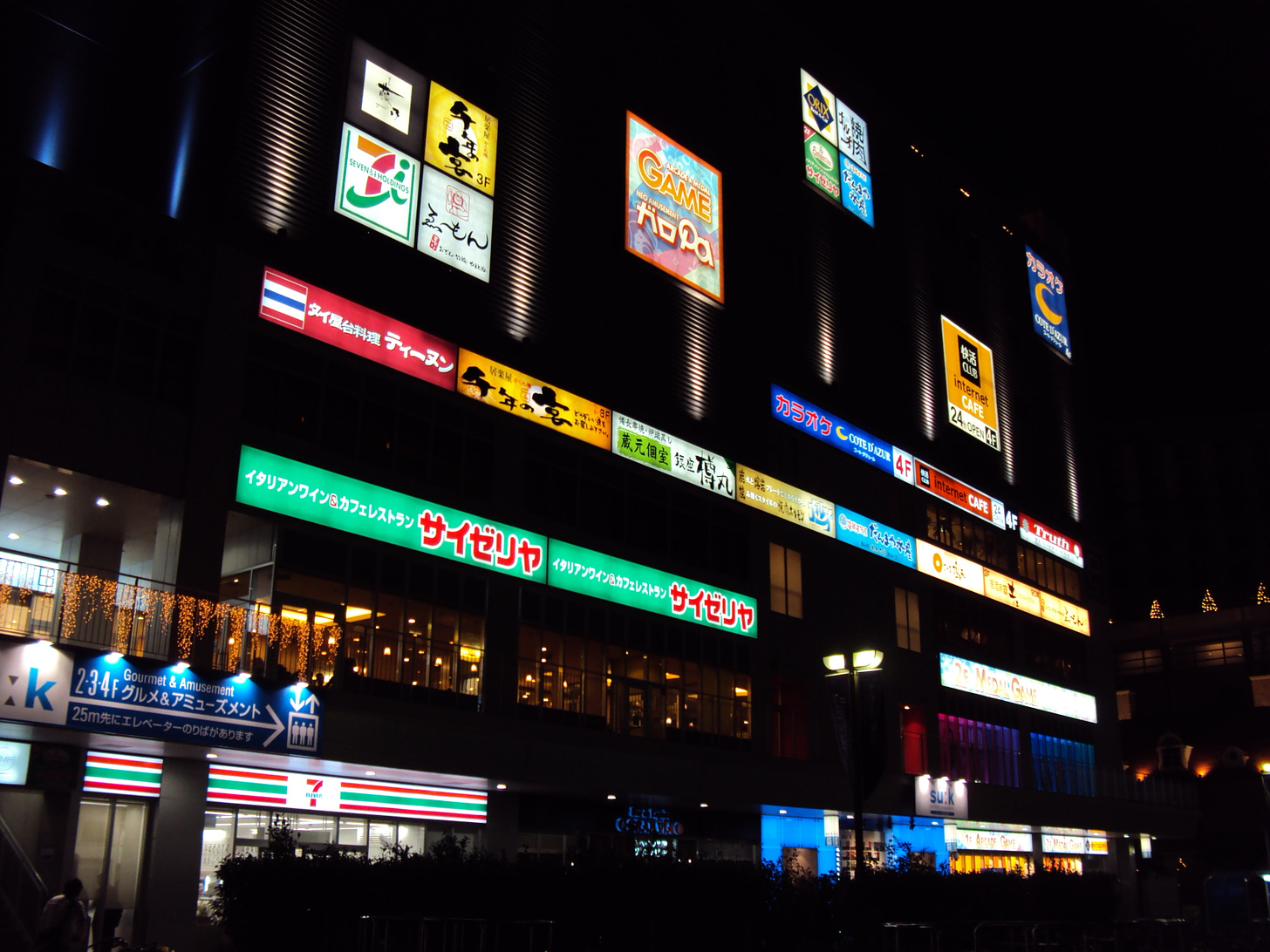 Nighttime image of a building with many brightly lit signs of various shops.