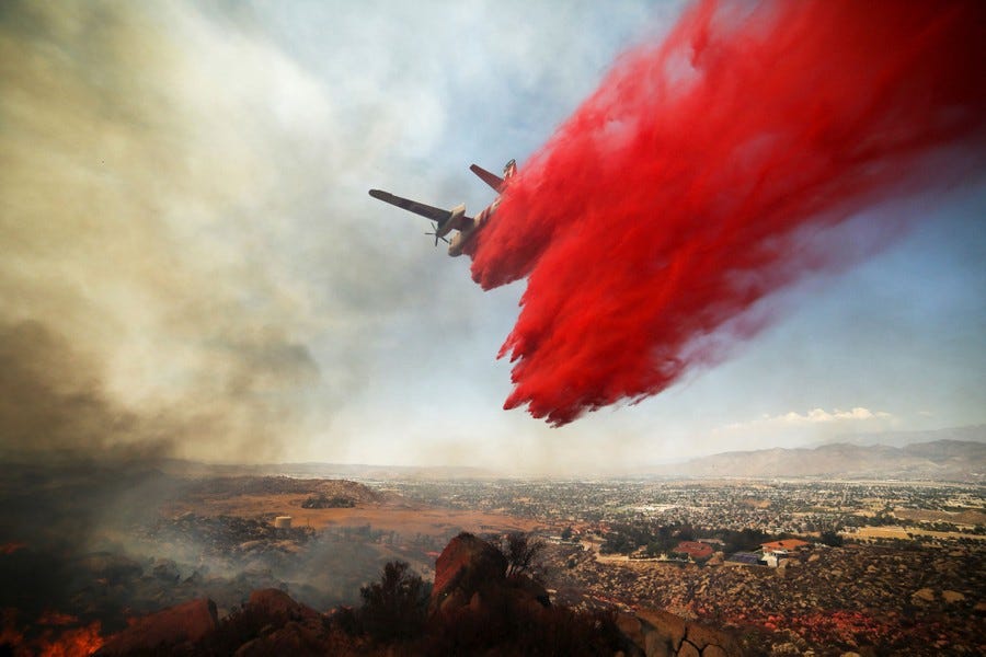 Fire retardant is dropped on a fire by a low-flying aircraft.