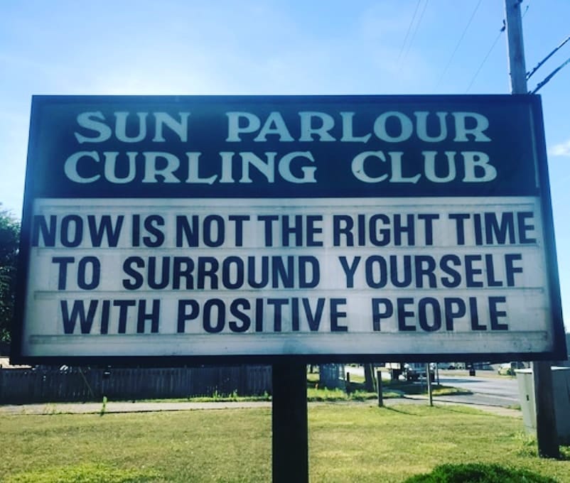 The marquee sign of the Sun Parlour Curling Club that reads "NOW IS NOT THE TIME TO SURROUND YOURSELF WITH POSITIVE PEOPLE""