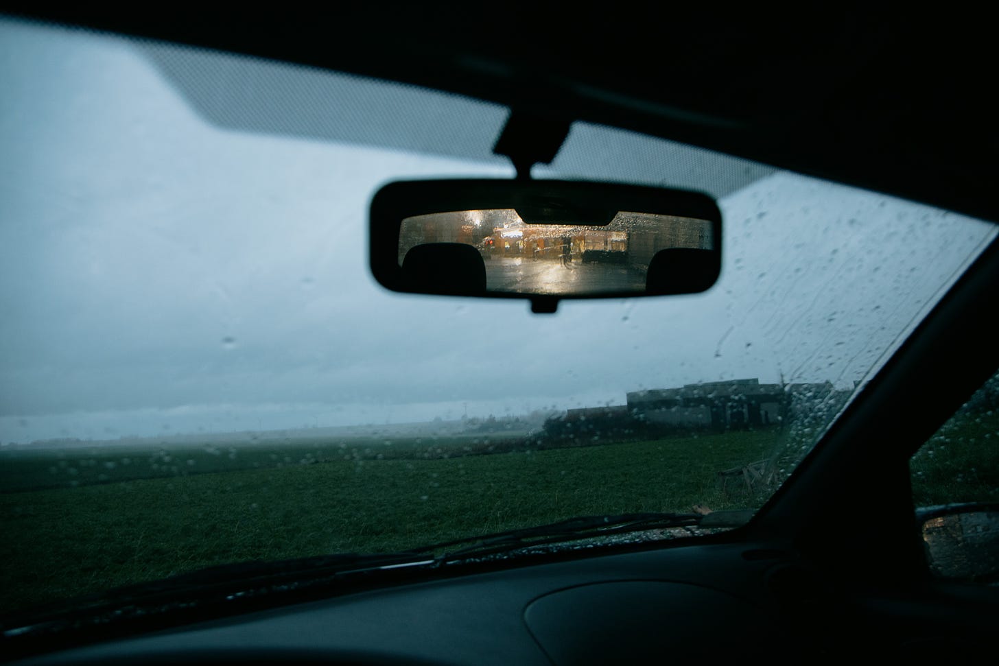 car window with water droplets and a rearview mirror.