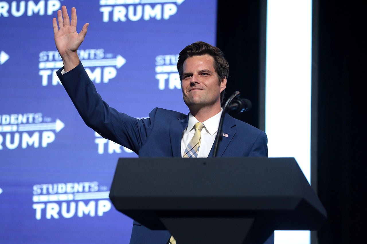Gaetz waving in front of a lectern. "Students for Trump" logo emblazon the background.