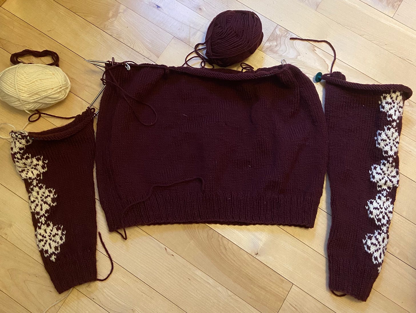 two sleeves, one half knit, and a torso, all on knitting needles, posed on the floor
