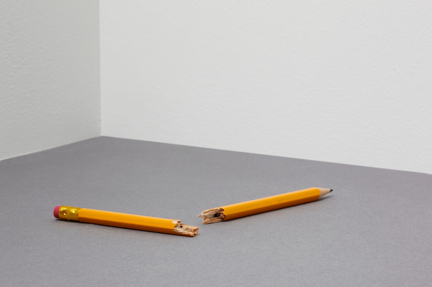 A single broken Number 2 pencil in an empty grey room