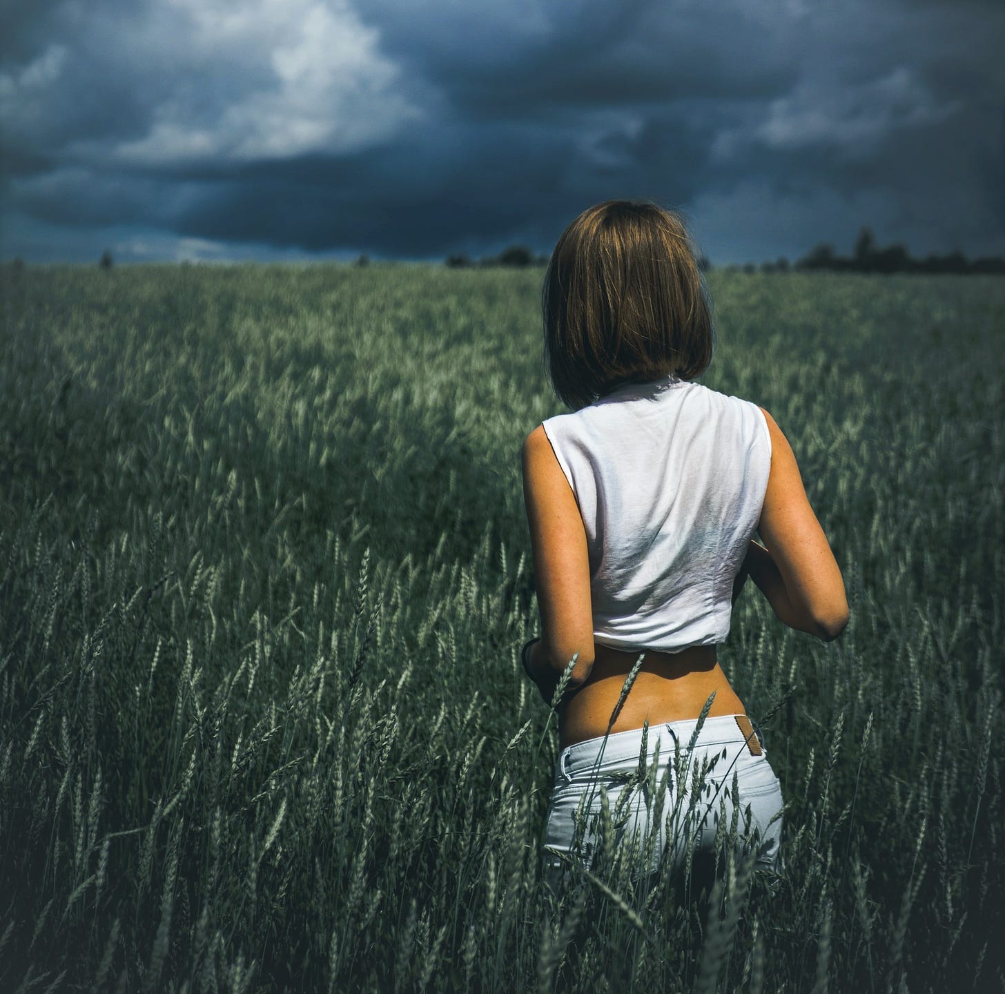 girl with brown hair standing in field looking at stormy sky